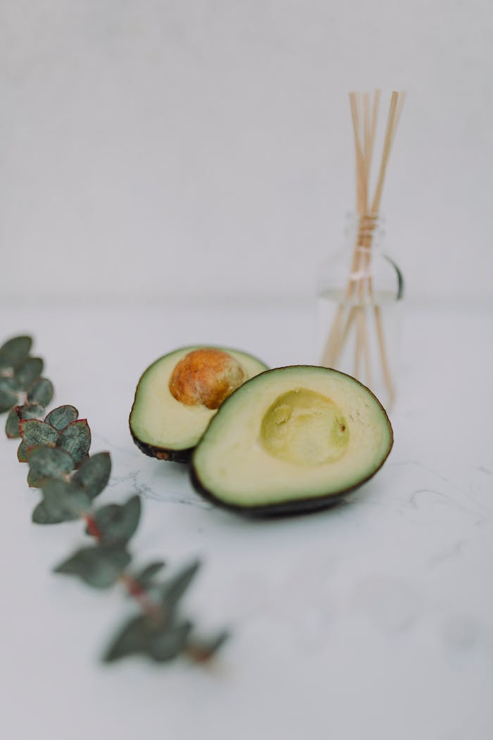 A serene still life featuring sliced avocado with eucalyptus leaves and a reed diffuser.